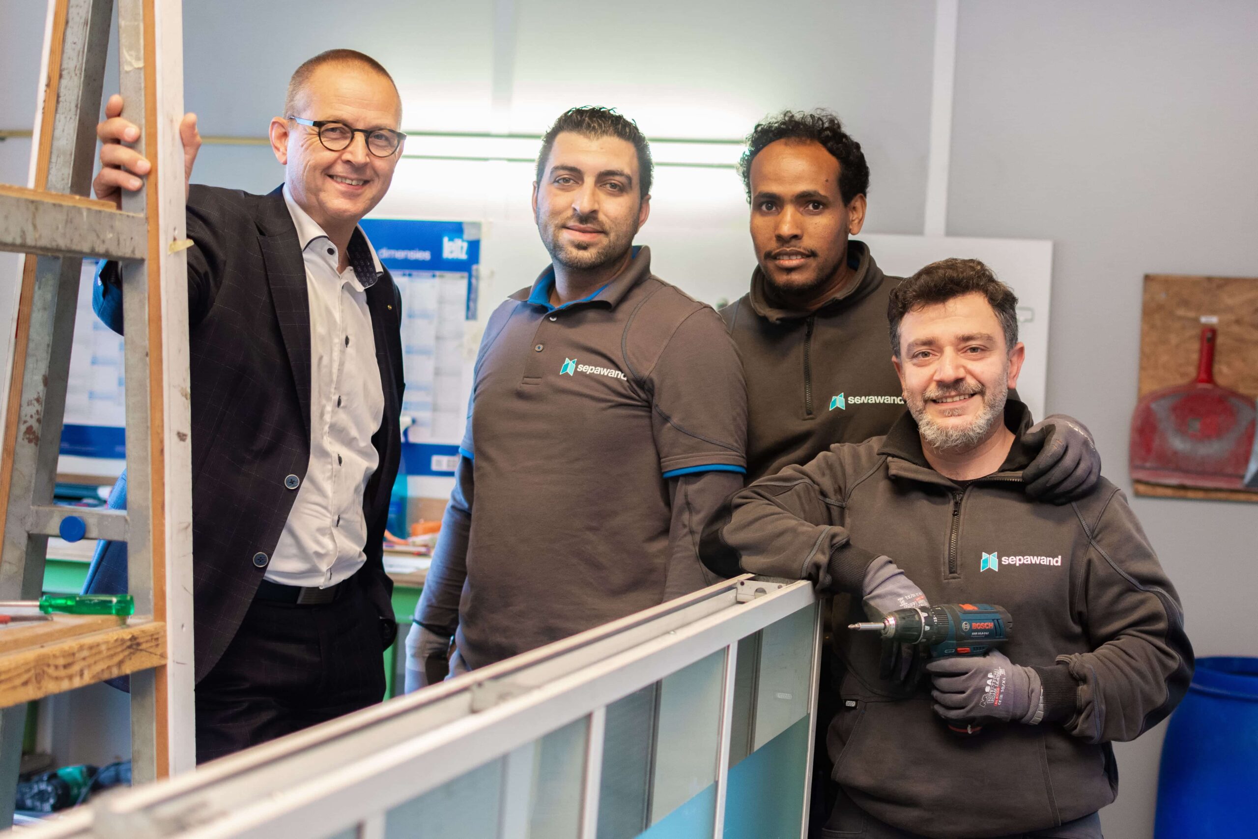 A businessman posing with three construction workers in matching uniforms inside a workshop.